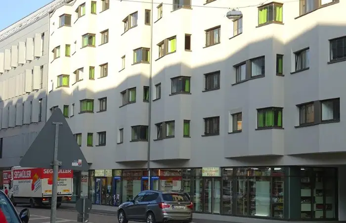 Wohn- und Geschäftshaus mit hellgrauer Fassade und Läden im Erdgeschoss.